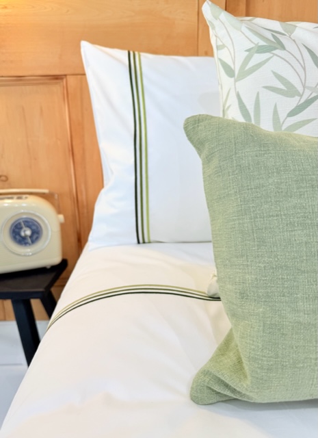 Doppelbett mit weisser Bettwäsche  und 3 grünen Streifen
