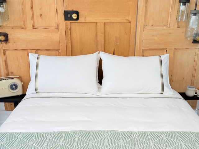 Doppelbett mit weisser Bettwäsche  und 3 grünen Streifen