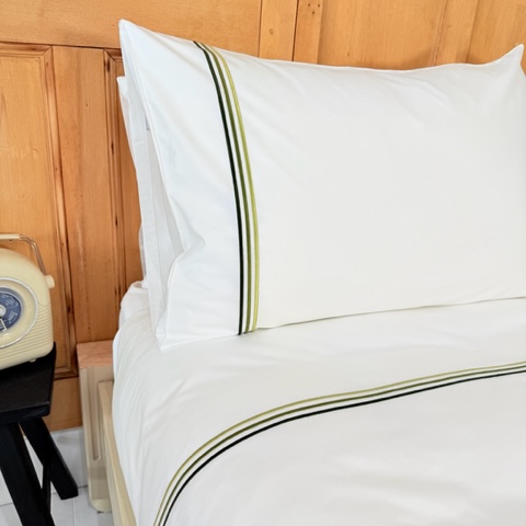 Bett mit weisser Bettwäsche  und 3 grünen Streifen